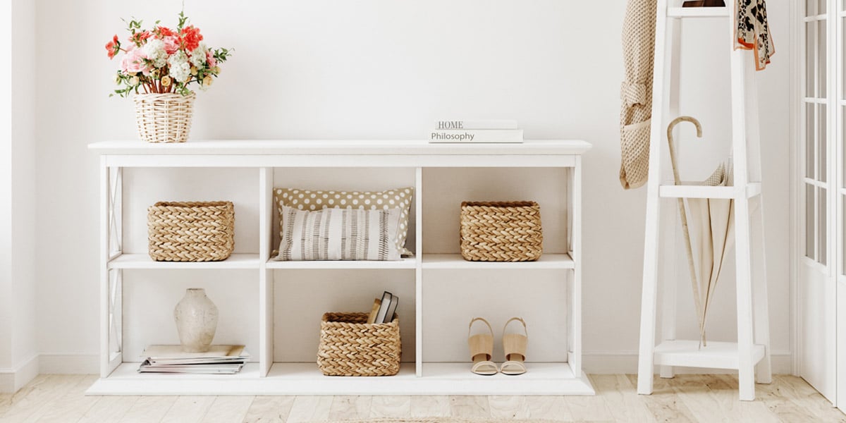 A bright entryway with a shelf that holds woven baskets and cut flowers, all in neutral colors.